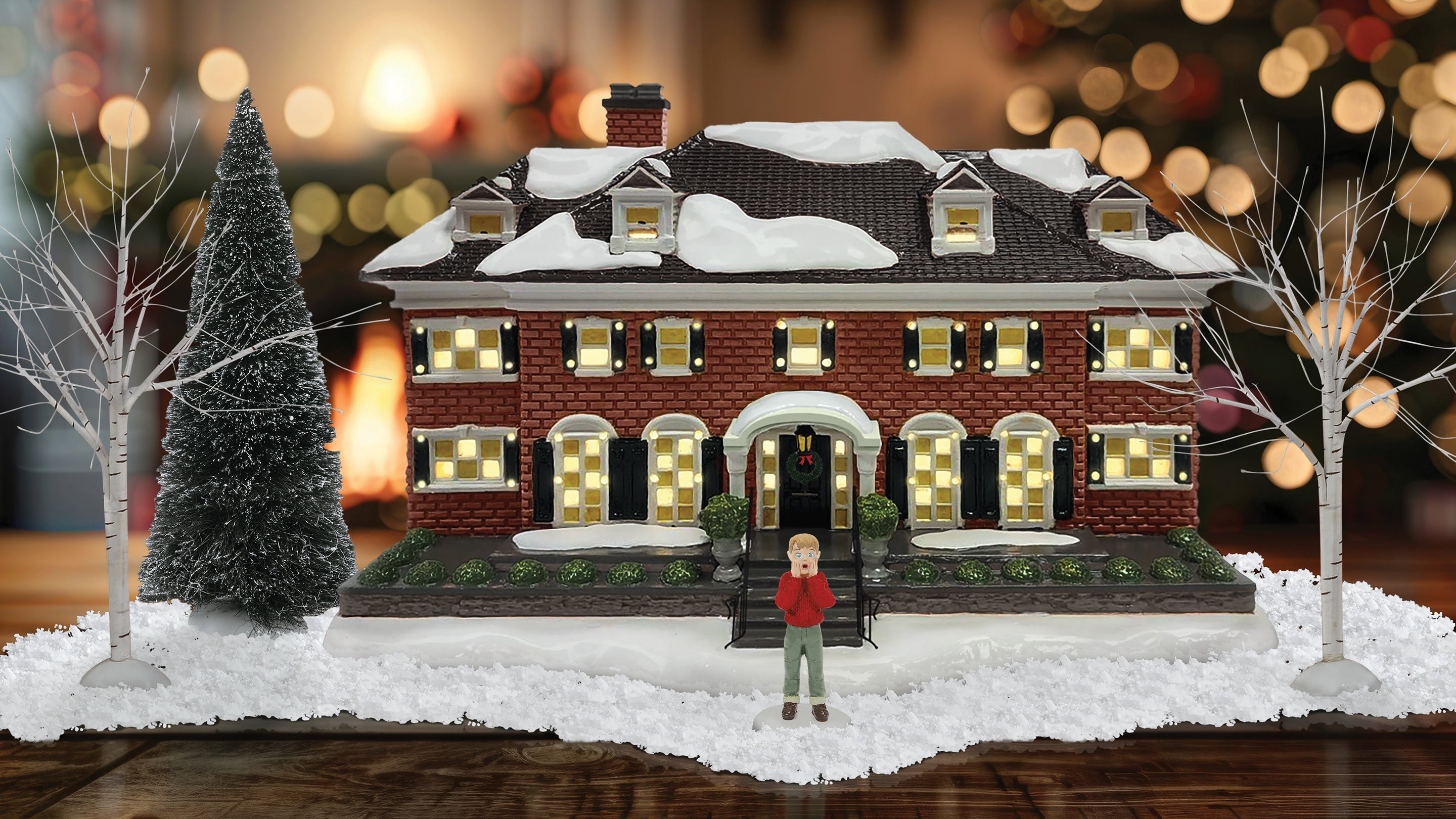 Model of a snowy house with a person standing in front, surrounded by trees and lights.