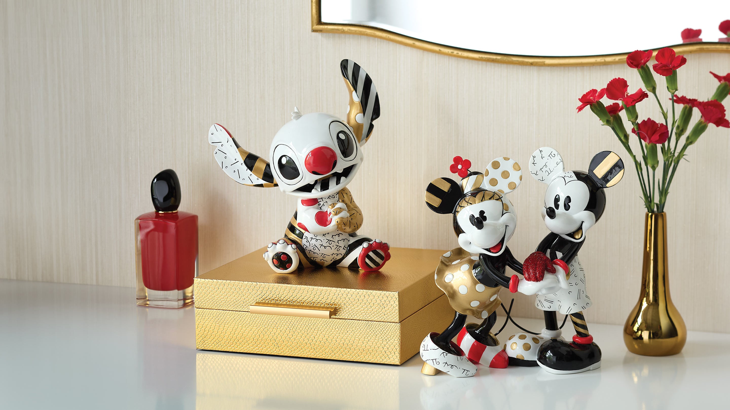 Two decorative figurines resembling cartoon characters on a table with a vase of flowers and nail polish in the background.