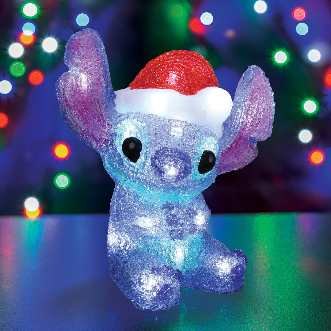 Colorful LED light-up character figure with a Santa hat against a blurred Christmas lights background