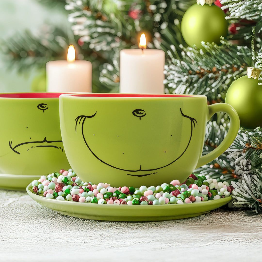 Green mugs with smiley faces on a saucer with Christmas decorations and candles.