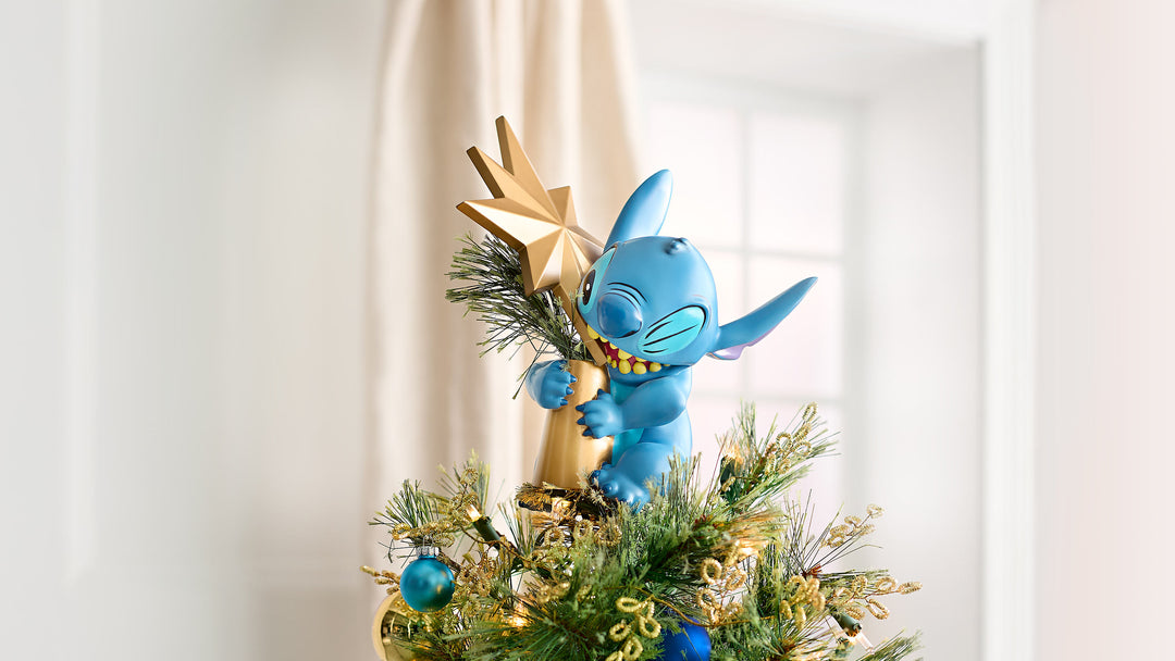 Blue cartoon character figurine on a decorated Christmas tree with gold and green ornaments.